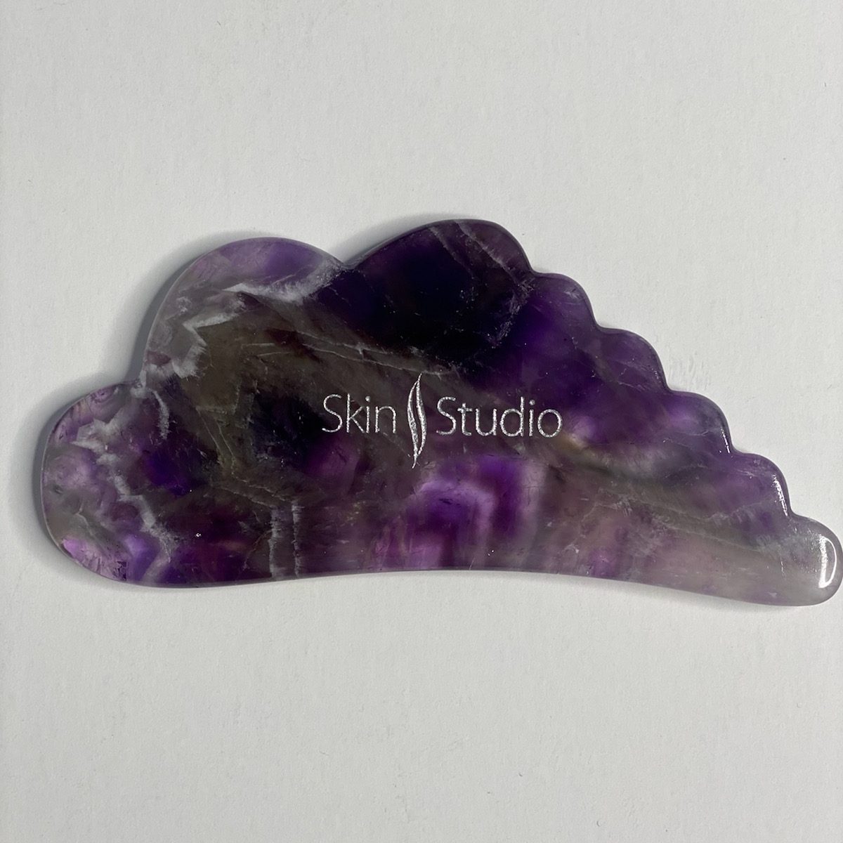 Gua sha tool made out of amethyst & Skin Studio Boston logo on top of it